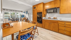 A modern kitchen with wooden cabinets, a microwave, and a dining area with a wooden table and chairs. - 25% Off Sept WkDays Great 4 Families, Walk 2 Beach (Ventura)