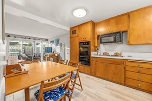 A modern kitchen with wooden cabinets, a microwave, and a dining area with a wooden table and chairs.