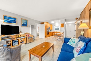 A living room with a TV, wooden furniture, a dining area, and a kitchen.