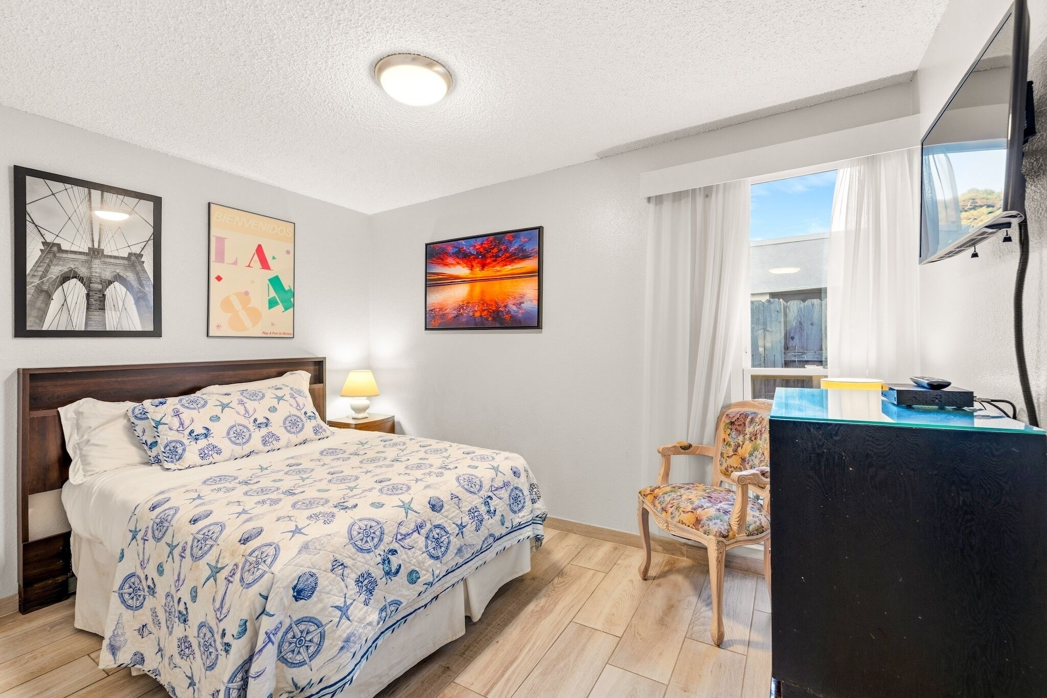Una habitación de hotel con cama, escritorio, silla y obras de arte en las paredes.