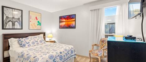 Una habitación de hotel con cama, escritorio, silla y obras de arte en las paredes.