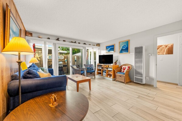 A living room with a sofa, coffee table, TV, and wicker chairs.