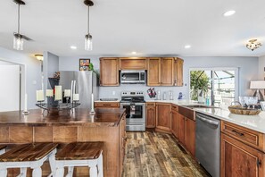 Een moderne keuken met houten kasten, roestvrijstalen apparatuur en een centraal kookeiland met krukken.