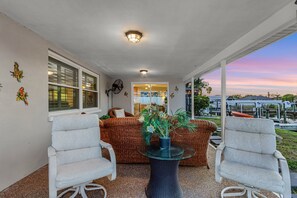 A covered patio area with two white chairs, a round table with a potted plant, and a view of the outdoors. - Beautiful home located on the canal w/gulf access, in ground pool, & wifi (Cape Coral)