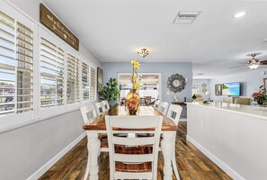 A dining area with a long table, white chairs, a vase with yellow flowers, and a wall-mounted sign. - Family-Friendly Cape Coral Home with Heated Pool & Canal Views (Cape Coral)