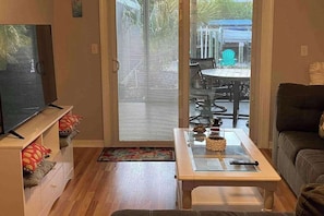 A living room with a TV, a glass coffee table, a sofa, and a sliding glass door leading to an outdoor patio. - Boat, Swim and Relax at Your Private Gulf Access Retreat (Saint James City)