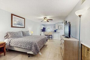 Quarto com cama, escrivaninha, cadeira, televisão e ventoinha no teto.