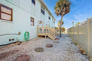 Ein Wohngebäude mit einer Holzterrasse, einer Palme und einem Schotterweg.