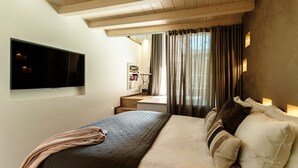 Une chambre à coucher avec un lit, un téléviseur fixé au mur, un bureau et une fenêtre avec des rideaux.