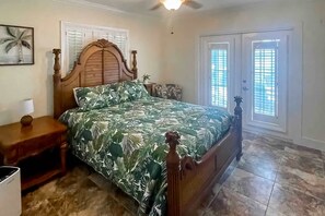 Ein Schlafzimmer mit einem hölzernen Bett, einem Nachttisch, einem Deckenventilator und einem Fenster mit Rollläden.