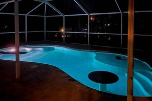 Ein Pool mit einem außergewöhnlichen, gitarrenförmigen Design, umgeben von einer Glaskonstruktion mit Blick auf die beleuchtete Stadt.