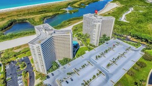 Ein Hochhaus-Hotel mit Parkplatz, umgeben von Grünflächen und einem Strand.