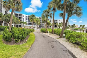 A pathway leading to a modern building with multiple floors, surrounded by well-maintained greenery and palm trees. - Spacious condo with water views, tennis, hot tub & pool - ideal for relaxation (Marco Island)