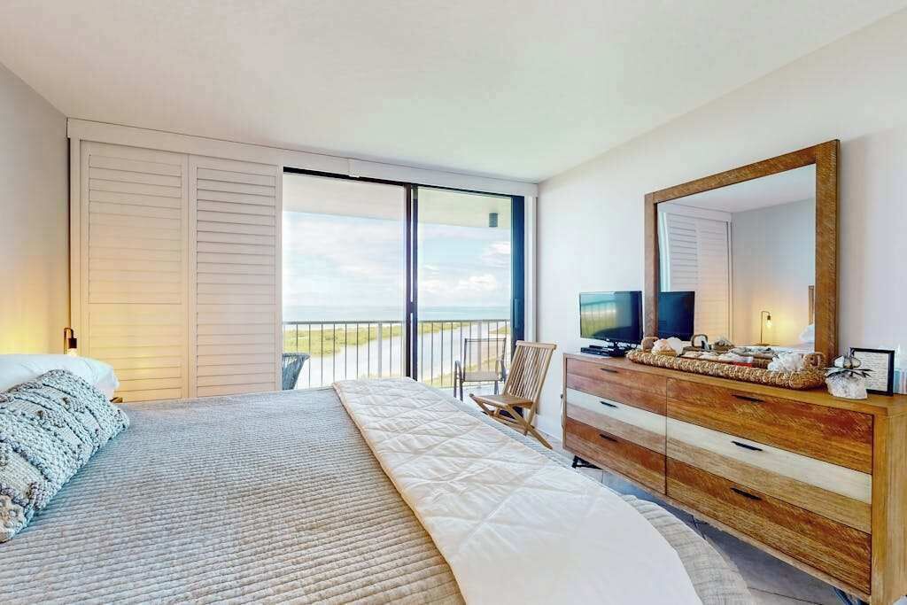 A bedroom with a bed, a dresser, a television, and a balcony with a view.