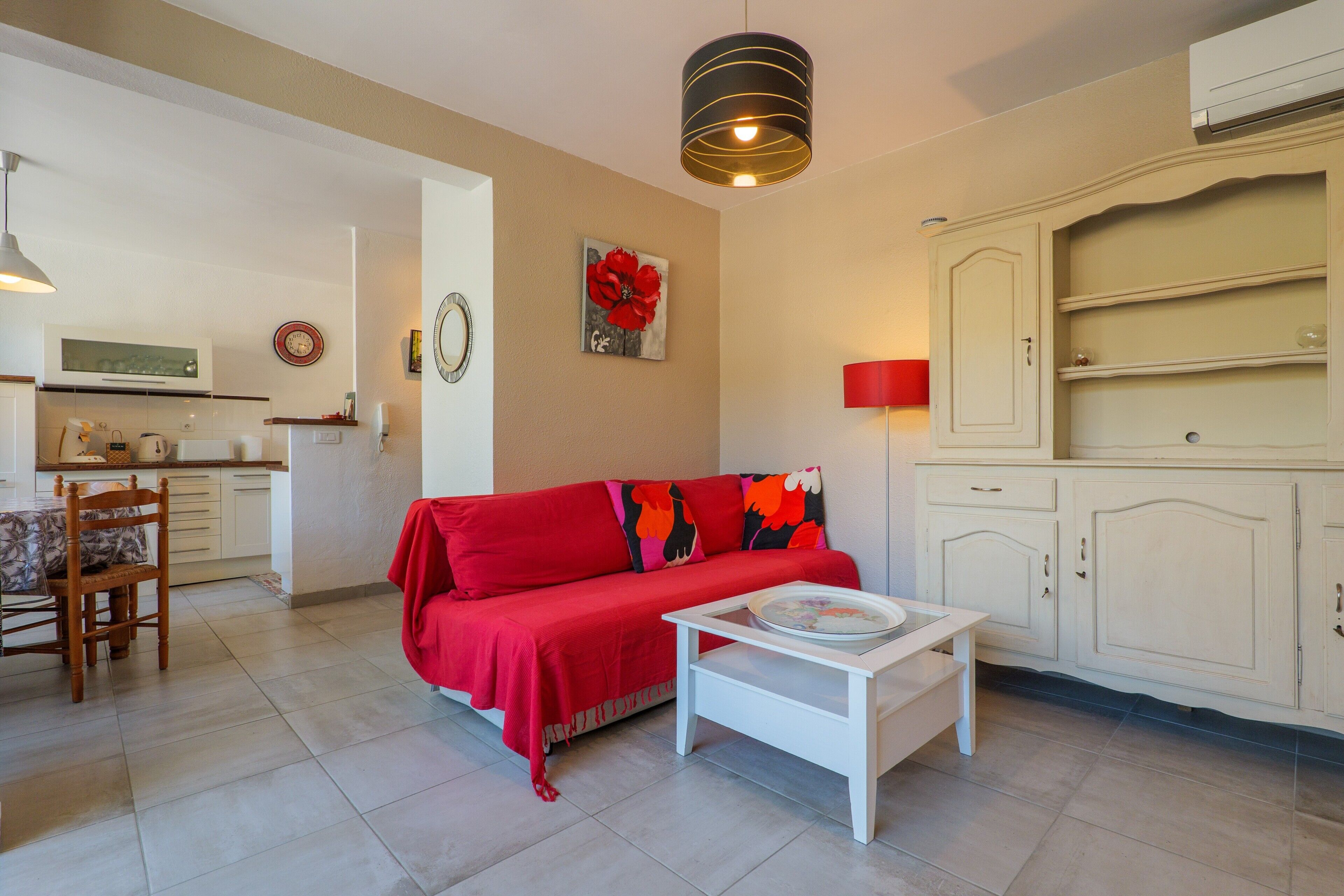 A living room with a red sofa, a white coffee table, and a kitchen area in the background.