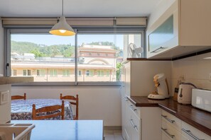 Eine Küche mit Blick auf ein Gebäude, einem Tisch mit Stühlen und einem Fenster mit Vorhang.