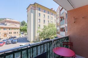 Ein Balkon mit einem roten Tisch und Stühlen, mit Blick auf eine Straße mit geparkten Autos und Gebäuden.