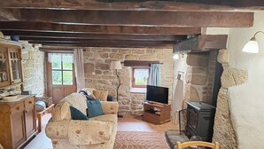A rustic interior with a stone wall, wooden furniture, a television, and a fireplace. - Delightful 1-bedroom cottage in tranquil Sainte Price Melrand perfect getaway (Melrand)