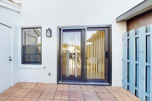 Un edificio blanco con puerta corredera de vidrio, una ventana con persianas y cerca de madera azul.
