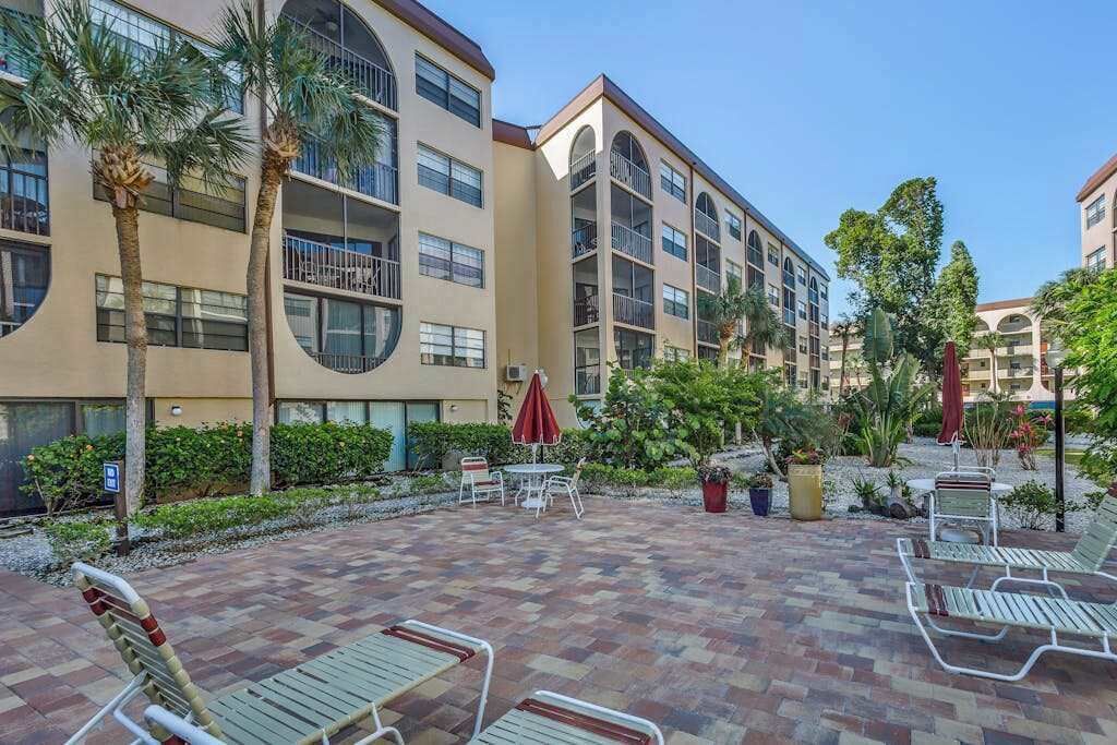 A courtyard with outdoor seating, palm trees, and a multi-story building with balconies.