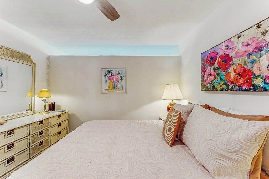 A bedroom with a bed, a dresser, a painting, and a ceiling fan.