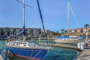 A marina with boats docked, a building with arched windows, and a clear sky. - Snowbird-friendly condo with hot tub, outdoor pool, tennis, dock, BBQ, & balcony (Marco Island)