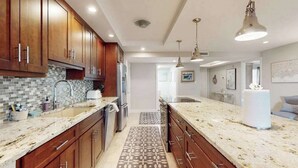A modern kitchen with wooden cabinets, granite countertops, and pendant lighting. - Spacious oceanfront condo with heated pool, pickleball, tennis, gym, & balcony (Marco Island)