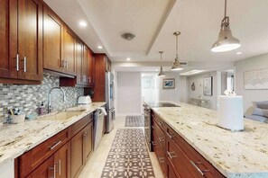 A modern kitchen with wooden cabinets, granite countertops, and pendant lighting. - Spacious oceanfront condo with heated pool, pickleball, tennis, gym, & balcony (Marco Island)