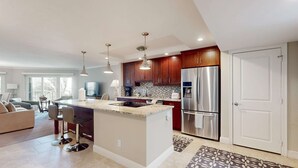 A modern kitchen with a central island, stainless steel appliances, and pendant lighting. - Spacious oceanfront condo with heated pool, pickleball, tennis, gym, & balcony (Marco Island)