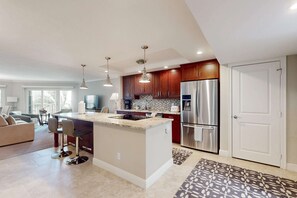 A modern kitchen with a central island, stainless steel appliances, and pendant lighting. - Spacious oceanfront condo with heated pool, pickleball, tennis, gym, & balcony (Marco Island)