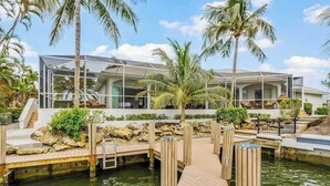 Een modern resort met een glazen gebouw, een houten steiger en palmbomen.