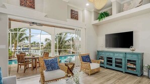 Un amplio salón con un televisor grande, muebles de mimbre y vistas a una piscina.