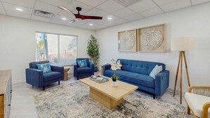 Een moderne woonkamer met een blauwe bank, twee fauteuils, een houten salontafel en een vloerlamp.