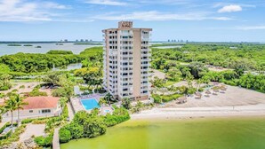 Een hoog hotel met zwembad, omgeven door weelderige begroeiing en een strand.