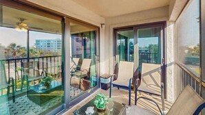 A balcony with glass doors, chairs, a small table, and a potted plant. - Coastal condo with shared pool, tennis court, and washer & dryer (Fort Myers Beach)