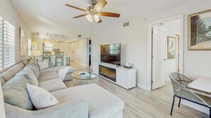 A modern living room with a sectional sofa, a flat-screen TV, a ceiling fan, and a dining area with a table and chairs. - Coastal condo with shared pool, tennis court, and washer & dryer (Fort Myers Beach)