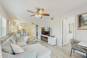 A modern living room with a sectional sofa, a flat-screen TV, a ceiling fan, and a dining area with a table and chairs. - Coastal condo with shared pool, tennis court, and washer & dryer (Fort Myers Beach)