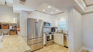 A modern kitchen with white cabinetry, stainless steel appliances, and a marble countertop. - Coastal condo with shared pool, tennis court, and washer & dryer (Fort Myers Beach)
