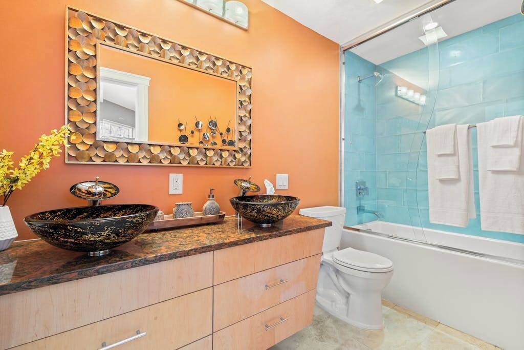 Un baño con un espejo grande, dos lavamanos sobre encimera, un inodoro y una ducha con mampara de vidrio.