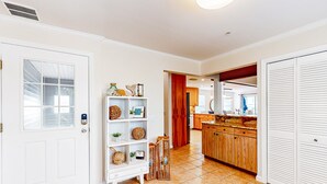 Ein Flur mit einer weißen Tür, einem weißen Regal mit Dekoration und einer Küchenzeile mit Holzschränken sowie einem gemusterten Teppich.
