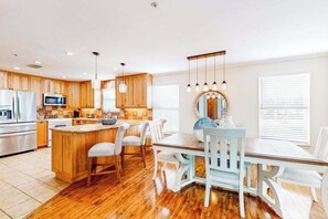 Una cocina con armarios de madera, una isla central y una zona de comedor con sillas blancas y una mesa.