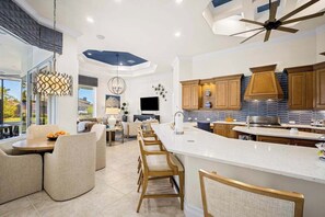 A modern kitchen with a large island, wooden cabinets, and a ceiling fan. - Luxe home near the water with private heated pool, pool spa, grill, firepit, AC (Marco Island)