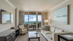 A hotel room with a sofa, a coffee table, a TV, a desk, and a balcony with a view of the ocean. - Gulf-front condo with pool, hot tub, & central AC - snowbird-friendly (Marco Island)