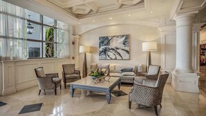 Eine großzügige Lobby mit hoher Decke, großen Fenstern und einer zentralen Sitzecke mit Couchtisch.