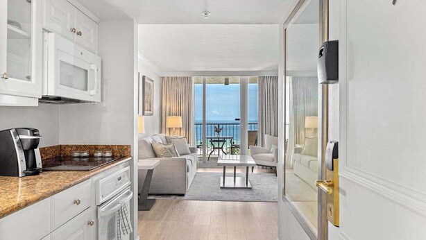 Ein modernes Hotelzimmer mit Küche, einem Balkon mit Aussicht, einer Sitzecke inklusive Sofa und Couchtisch sowie einem separaten Essbereich.