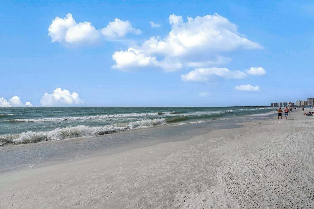 A beach with waves, a clear sky, and distant buildings.
