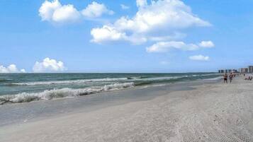 A beach with waves, a clear sky, and distant buildings.