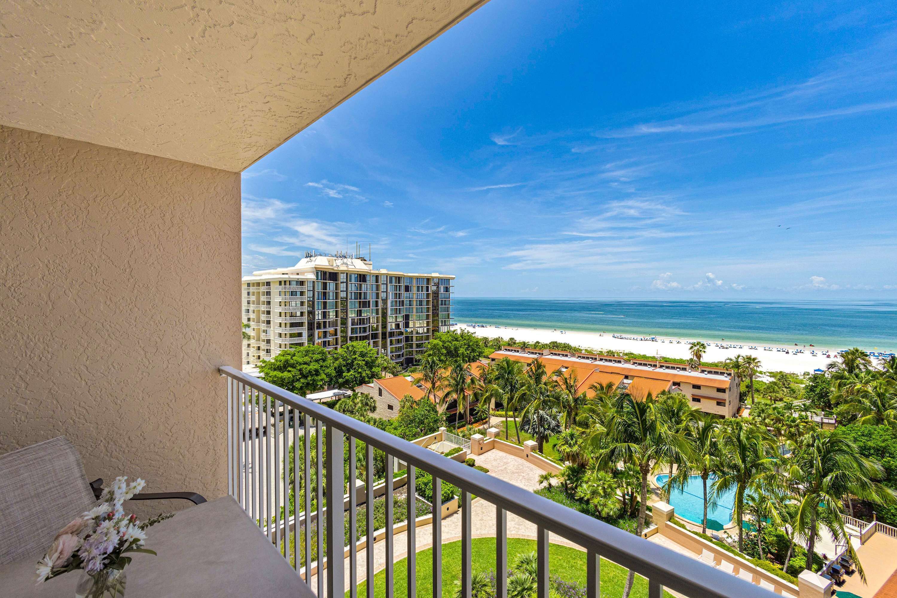 A balcony with a view of a beach, a pool, and a hotel building.