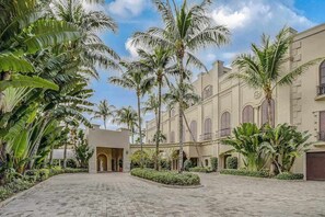Un patio con palmeras, un edificio con ventanas arqueadas y un sendero empedrado.