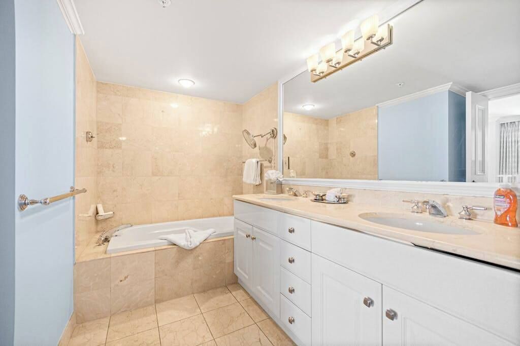 Une salle de bain avec une baignoire, deux lavabos, un grand miroir et un porte-serviettes.